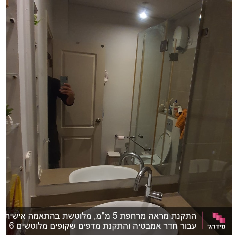 מראה גדולה מעל כיור בחדר אמבטיה